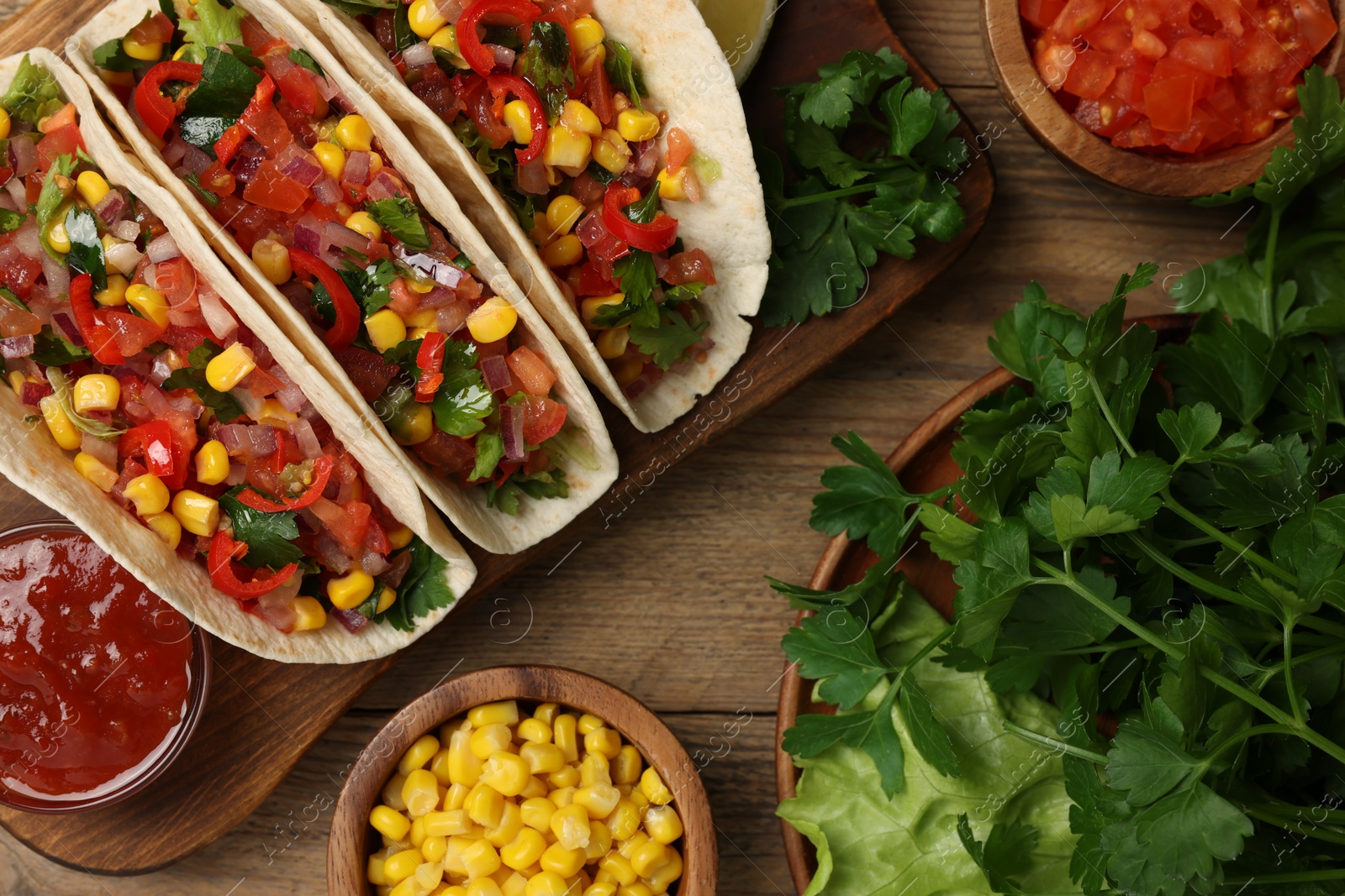 Photo of Tasty tacos with vegetables on wooden table, flat lay