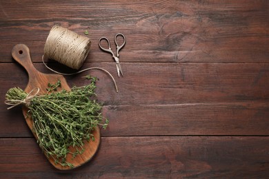 Photo of Bunch of aromatic thyme, scissors and twine on wooden table, flat lay. Space for text