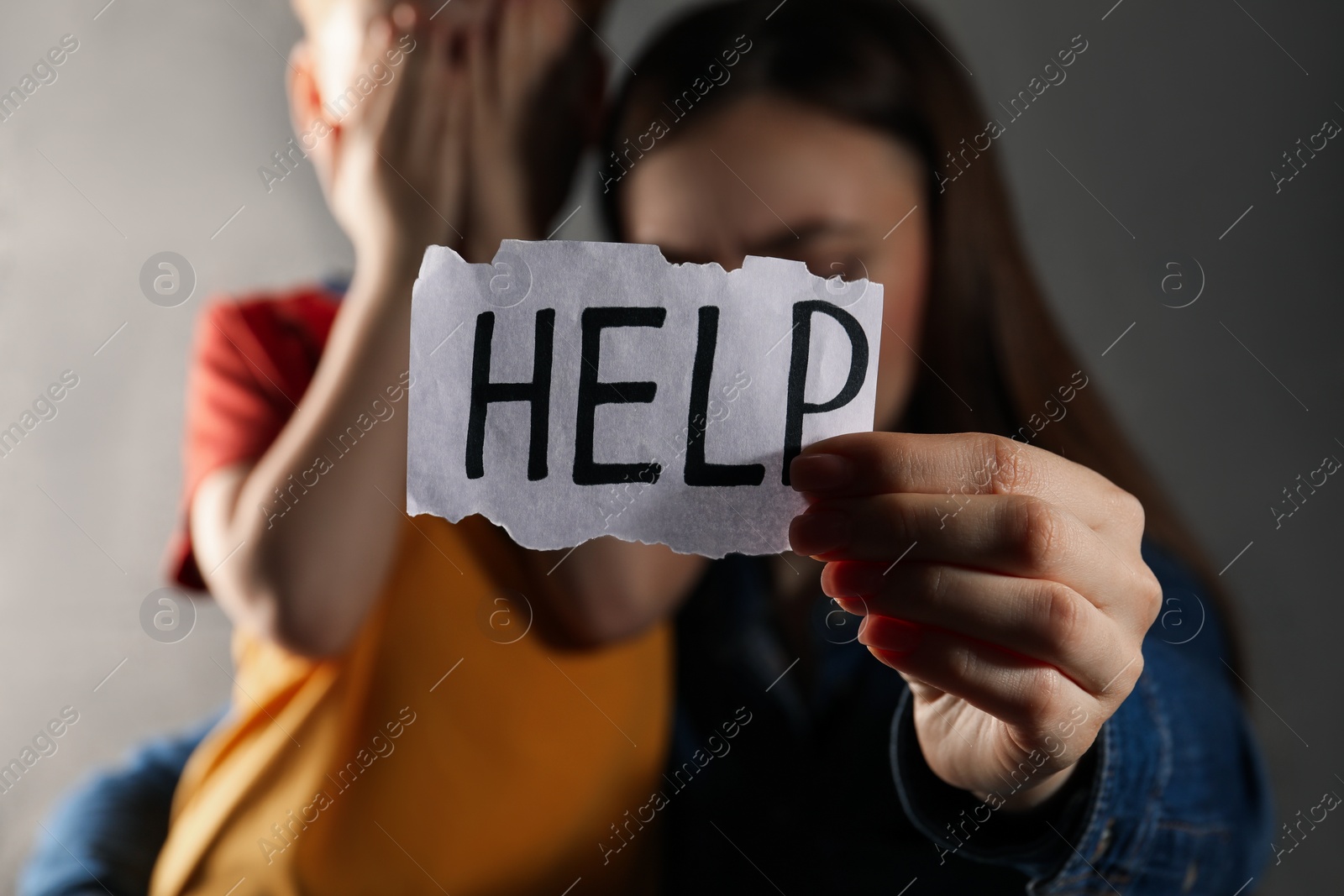 Photo of Little boy and mother holding piece of paper with word Help against light grey background, focus on hand. Domestic violence concept