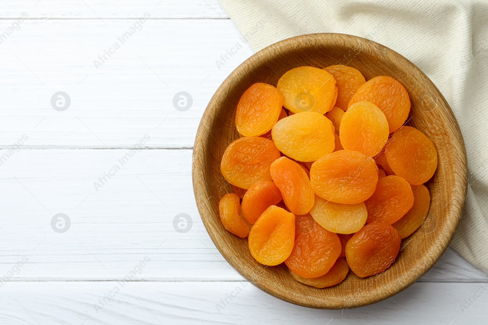 Photo of Bowl of tasty apricots and space for text on white wooden table, top view. Dried fruits