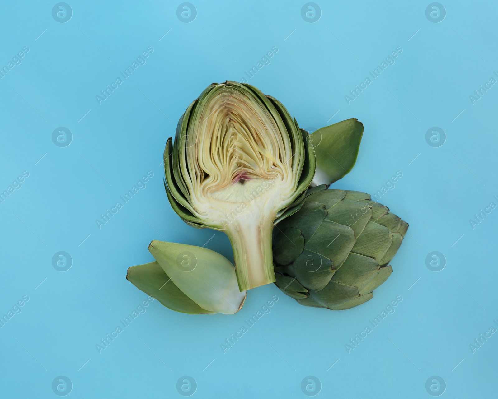 Photo of Cut fresh raw artichoke on light blue background, flat lay
