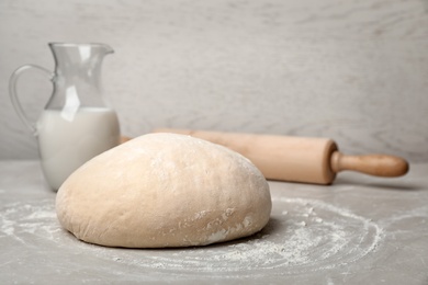 Raw wheat dough, pitcher with milk and rolling pin on table