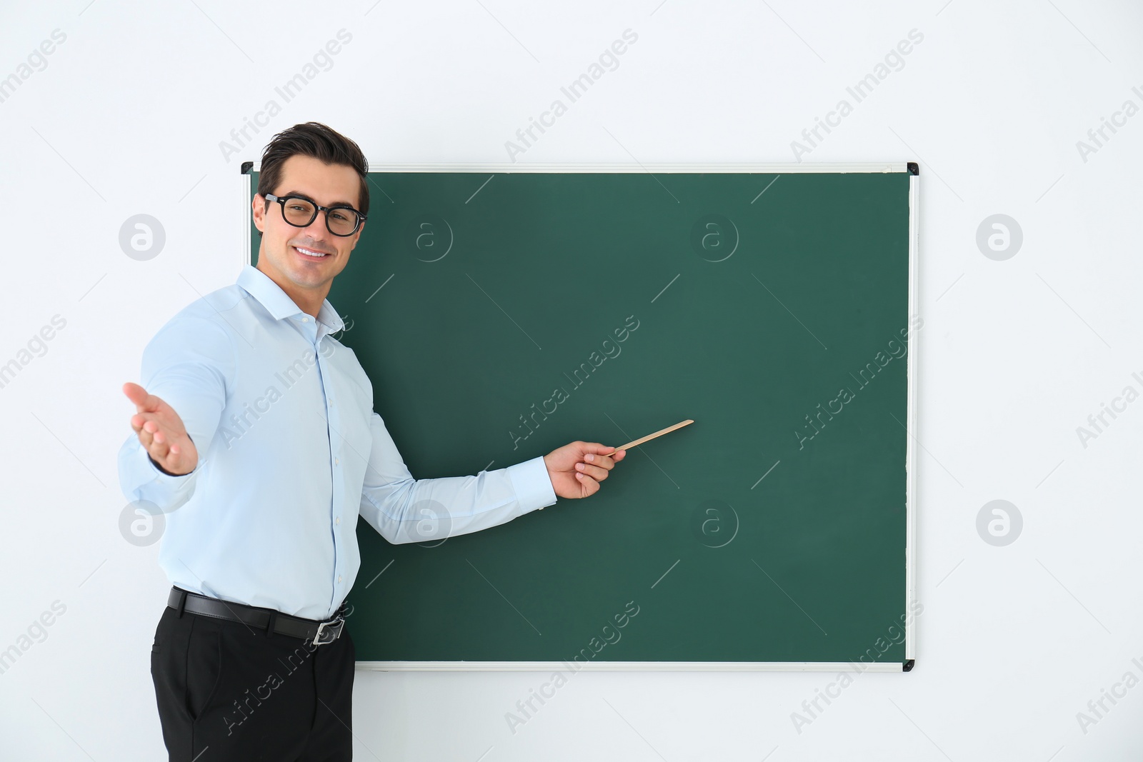 Photo of Young teacher with ruler near blank chalkboard in classroom. Space for text