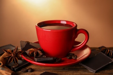 Photo of Cup of delicious hot chocolate, spices and coffee beans on wooden table