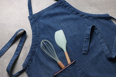 Photo of Stylish blue apron, spatula and whisk on grey table, top view