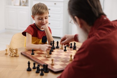 Photo of Little boy playing chess with his grandfather at table in room