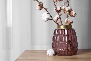 Cotton branches with fluffy flowers in vase on wooden table indoors. Space for text