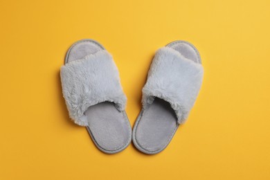 Photo of Pair of soft fluffy slippers on yellow background, top view