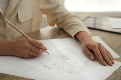 Photo of Woman drawing girl's portrait with pencil on sheet of paper at wooden table, closeup