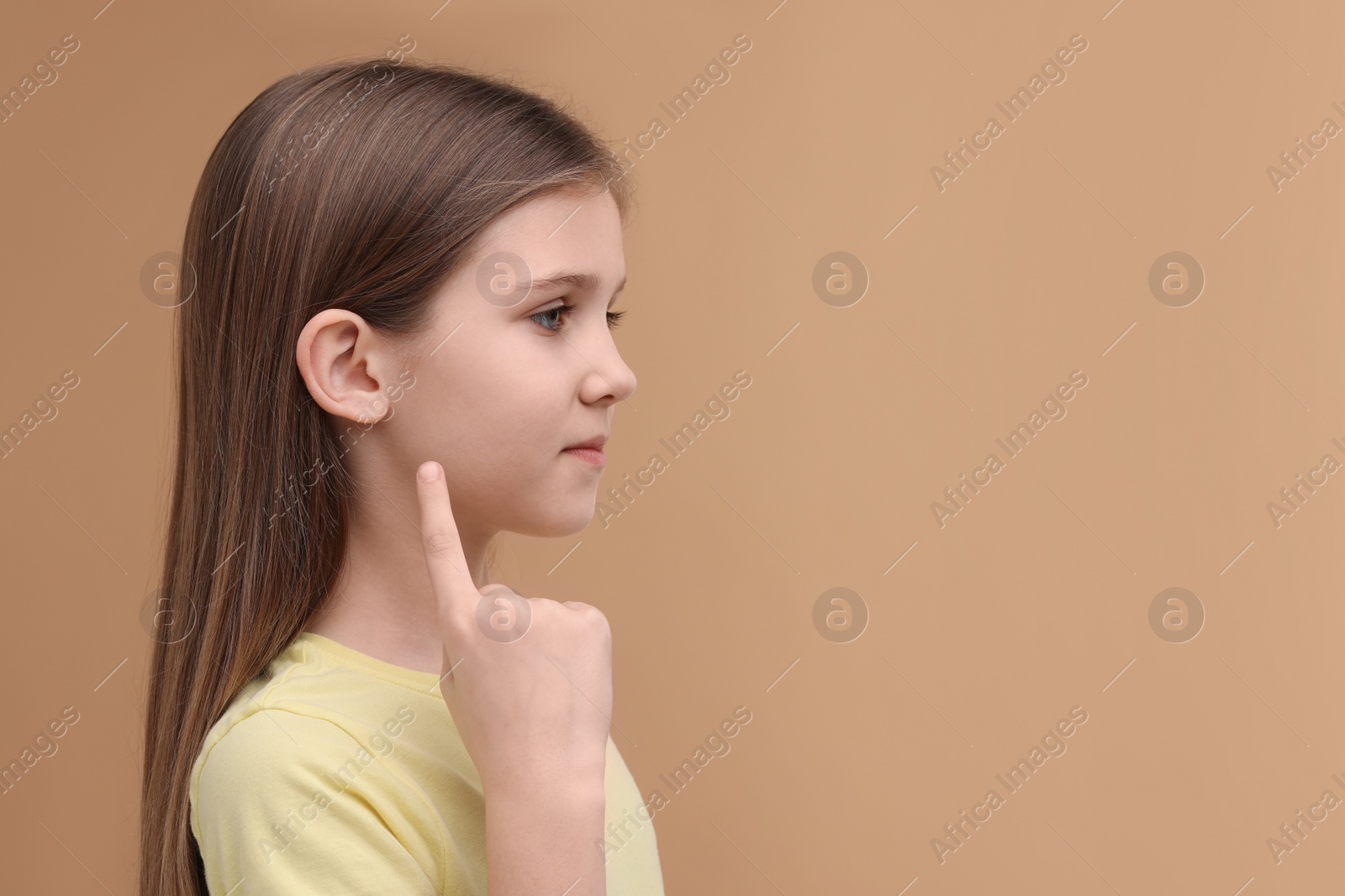 Photo of Hearing problem. Little girl pointing at ear on pale brown background, space for text