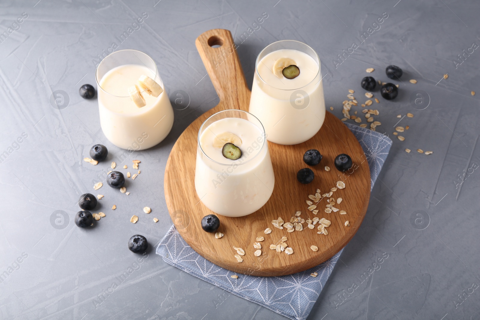 Photo of Tasty yogurt in glasses, oats and blueberries on grey table