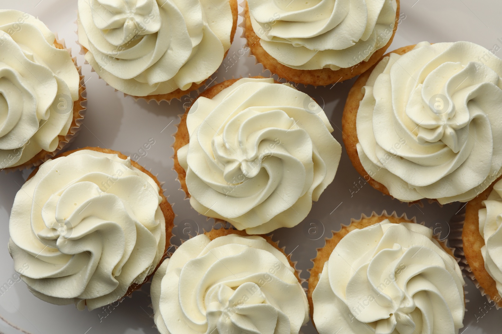 Photo of Tasty vanilla cupcakes with cream on plate, flat lay