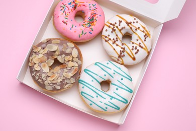 Box with different tasty glazed donuts on pink background, top view