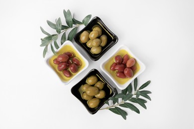 Bowls with different ripe olives and leaves on white background, flat lay