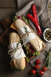 Photo of Delicious sandwiches with bresaola, lettuce and other products on wooden table, flat lay