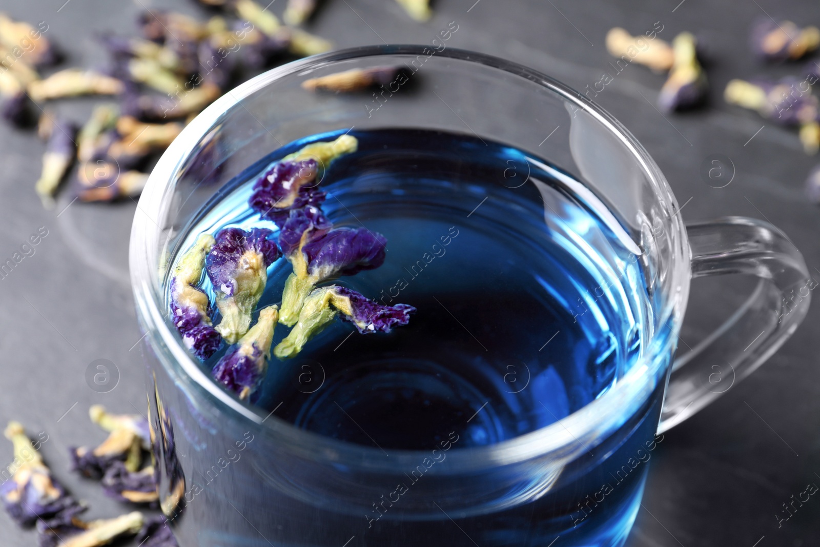 Photo of Glass cup of organic blue Anchan on black table, closeup. Herbal tea