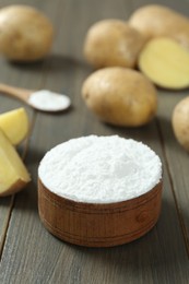 Photo of Bowl with starch and fresh potatoes on wooden table, space for text