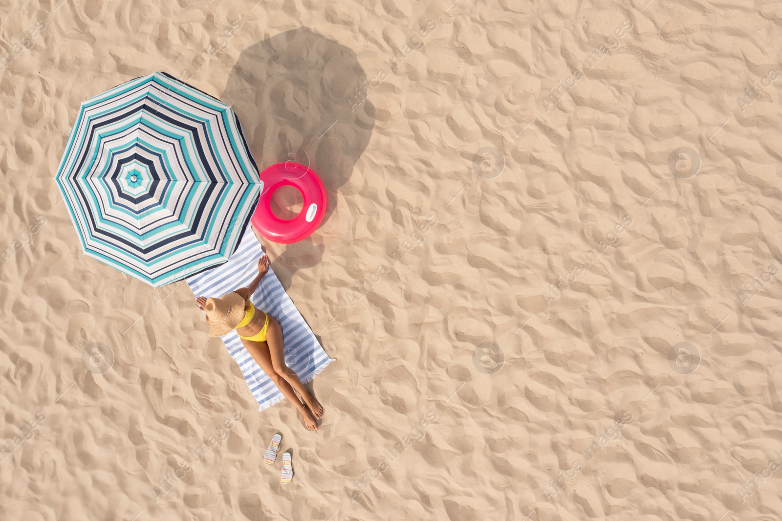 Image of Woman resting under striped beach umbrella at sandy coast, aerial view. Space for text