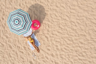 Woman resting under striped beach umbrella at sandy coast, aerial view. Space for text