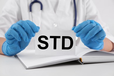 Doctor holding sheet of paper with abbreviation STD at white table, closeup