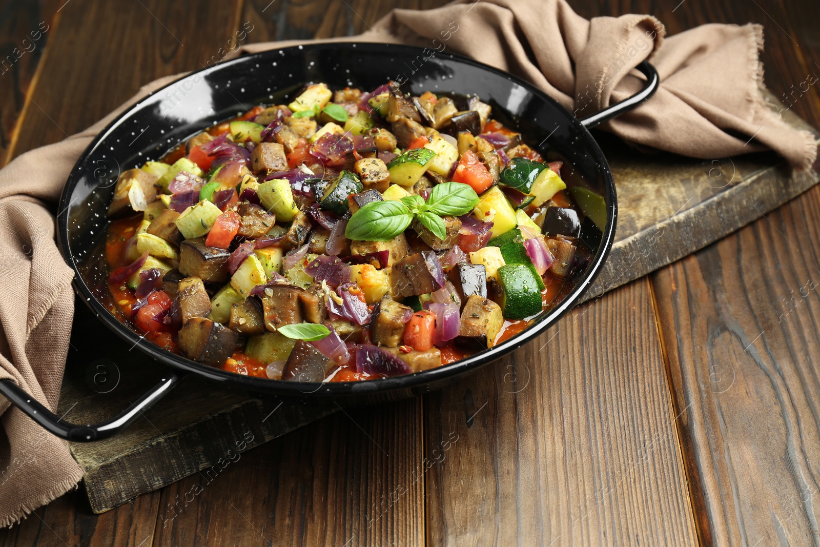 Photo of Delicious ratatouille in baking dish on wooden table, closeup