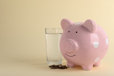 Photo of Water scarcity concept. Piggy bank, glass of drink and coins on beige background, space for text
