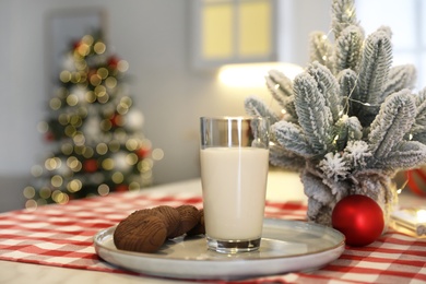 Photo of Glass of milk and chocolate cookies near little Christmas tree on table indoors