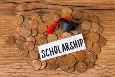 Photo of Paper with word Scholarship, graduation cap and coins on wooden table, flat lay
