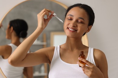 Smiling woman applying serum onto her face in bathroom