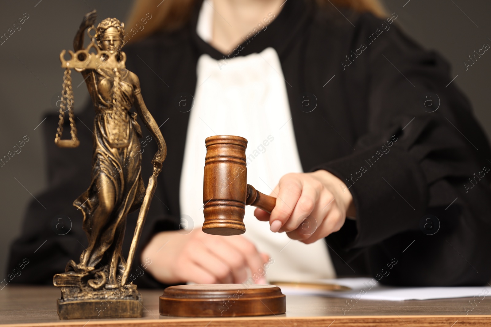 Photo of Judge striking mallet at wooden table indoors, selective focus. Figure of Lady Justice, closeup