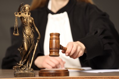 Photo of Judge striking mallet at wooden table indoors, selective focus. Figure of Lady Justice, closeup