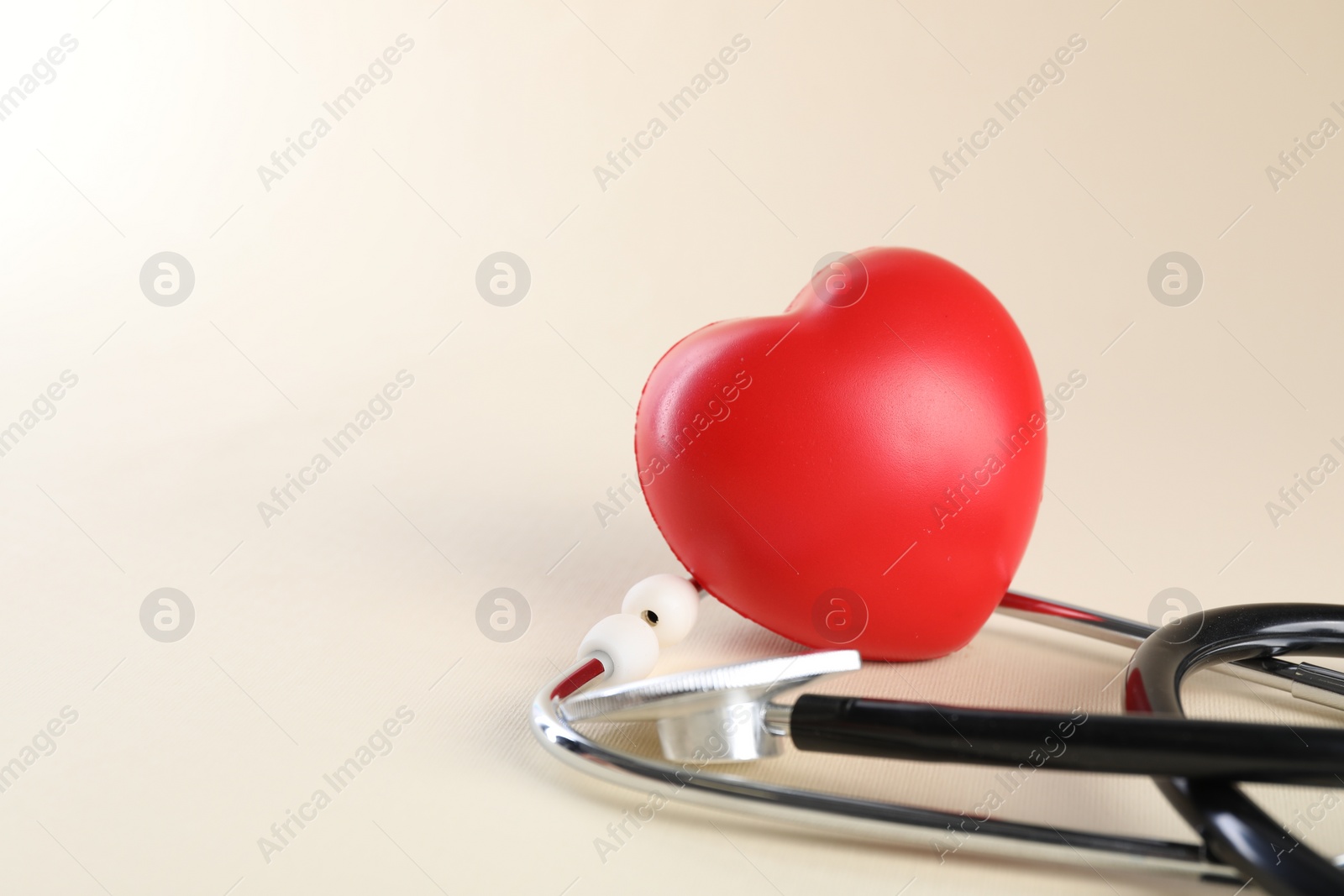 Photo of Stethoscope and red heart on beige background. Space for text