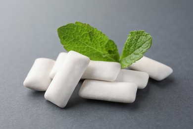 Photo of Tasty white chewing gums and mint leaves on grey background, closeup