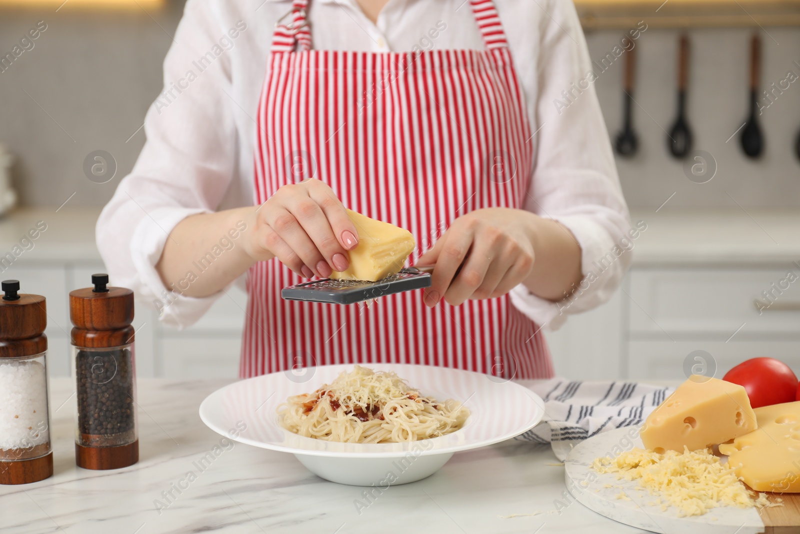 Photo of Woman grating cheese onto delicious pasta at white marble table in kitchen, closeup