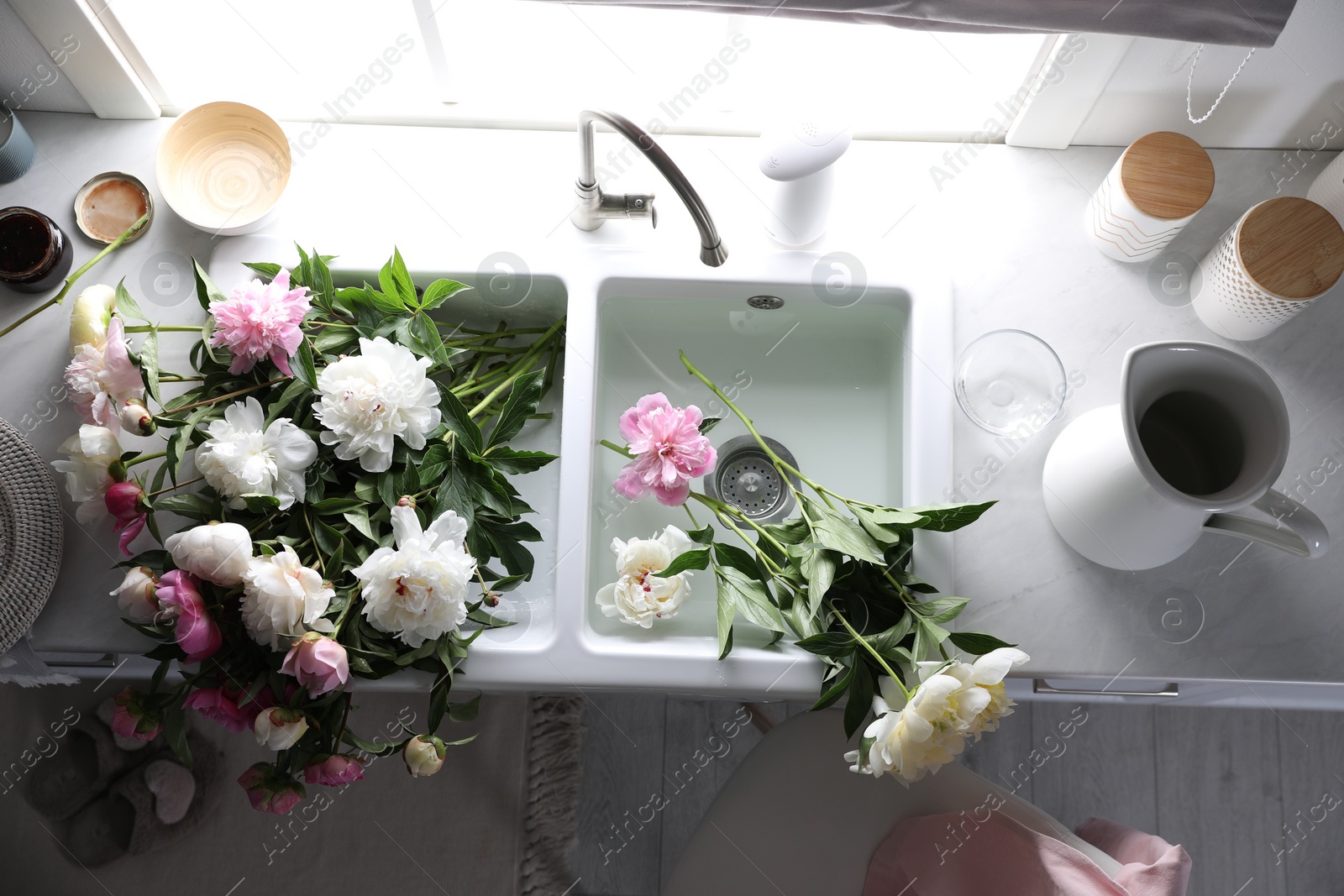 Photo of Bunch of beautiful peonies in kitchen sink, above view