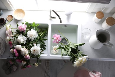 Photo of Bunch of beautiful peonies in kitchen sink, above view