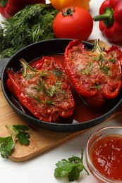 Photo of Tasty stuffed peppers in dish and ingredients on white table