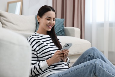 Photo of Happy young woman using smartphone at home