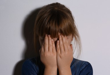 Photo of Abused little girl closing eyes near white wall. Domestic violence concept