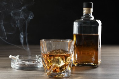 Photo of Alcohol addiction. Whiskey in glass, bottle, cigarettes and ashtray on wooden table