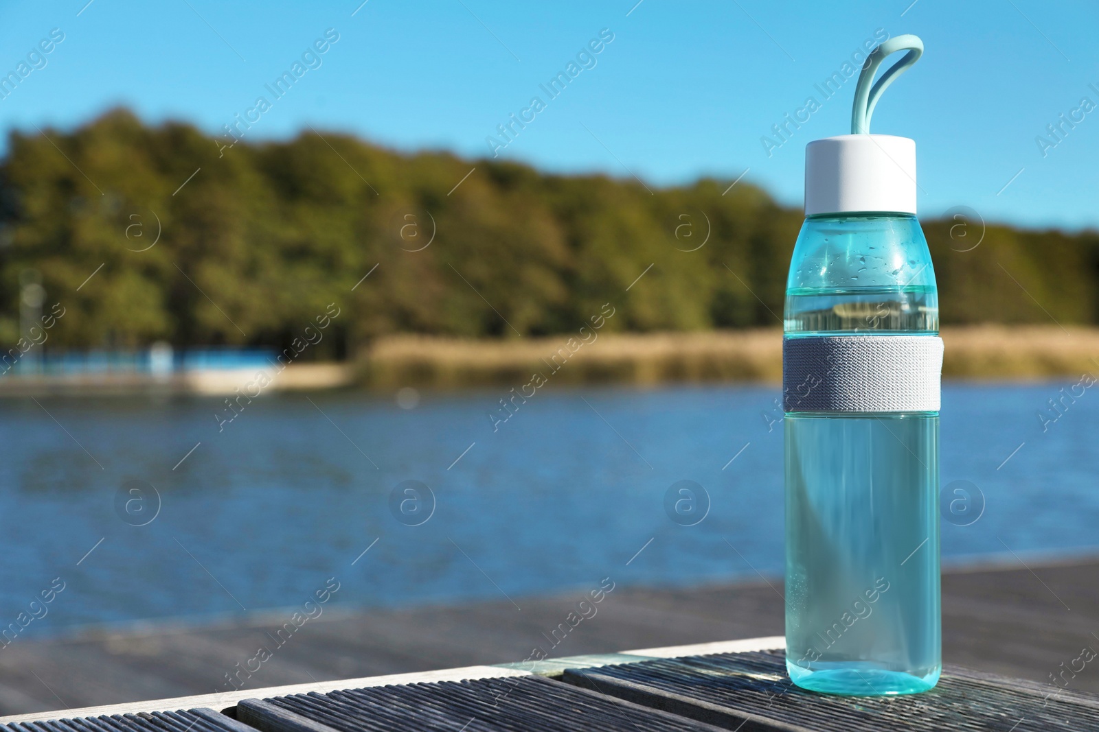 Photo of Glass bottle with water on wooden pier near river outdoors. Space for text