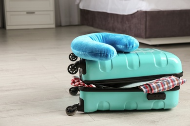 Suitcase with clothes and travel pillow in bedroom