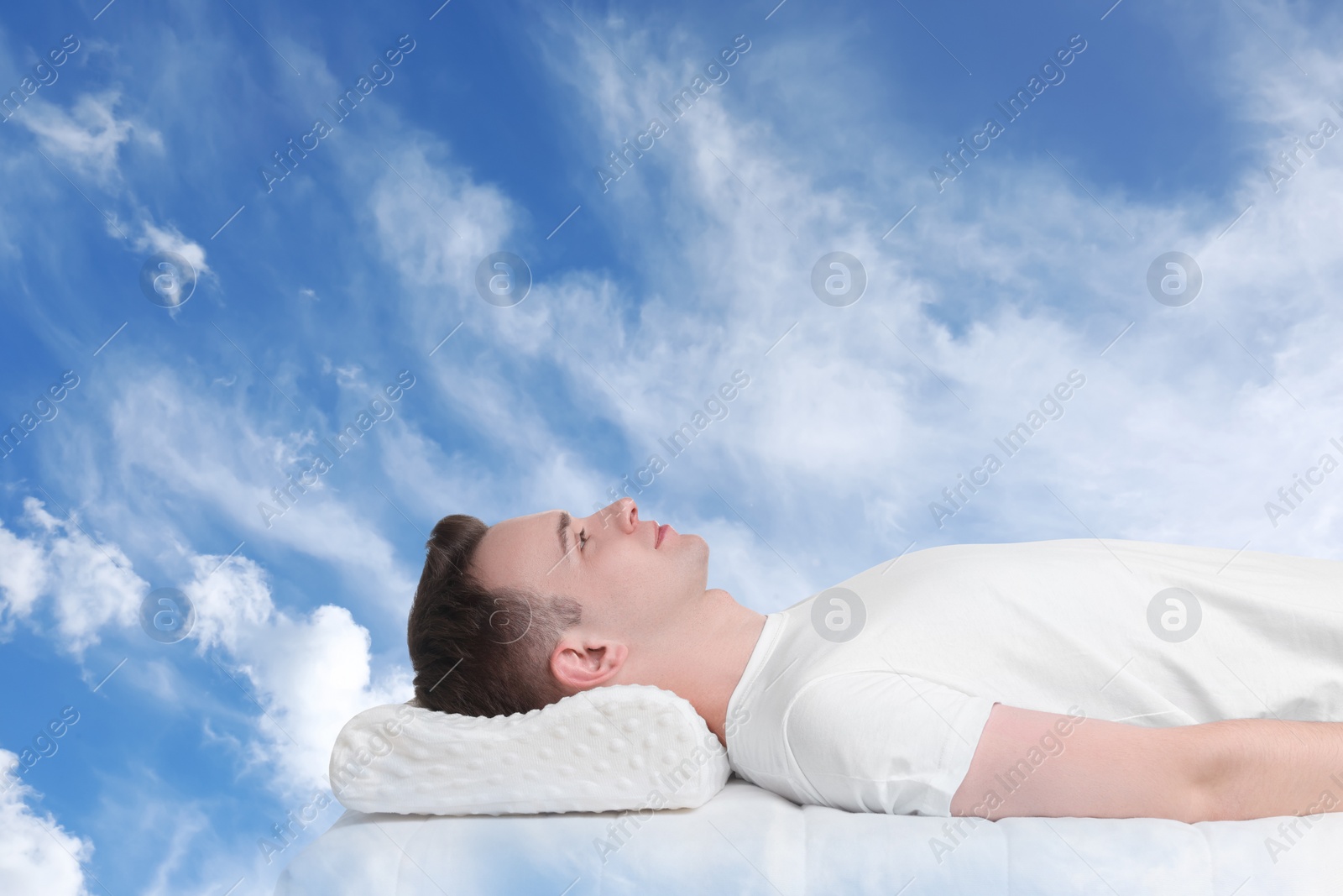 Image of Man lying on orthopedic pillow against blue sky