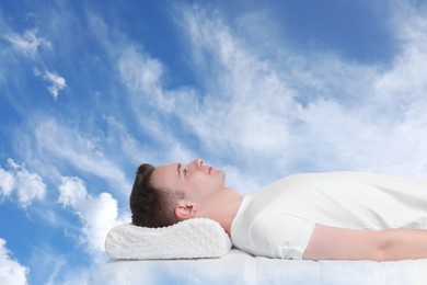 Man lying on orthopedic pillow against blue sky