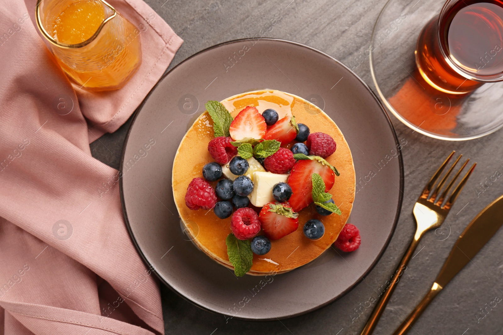 Photo of Delicious pancakes with fresh berries, honey and butter served on grey table, flat lay