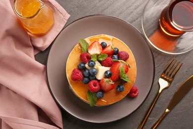 Delicious pancakes with fresh berries, honey and butter served on grey table, flat lay