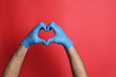 Photo of Doctor in medical gloves making heart with hands on red background, closeup. Space for text