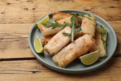 Photo of Plate with tasty fried spring rolls, arugula and lime on wooden table, closeup