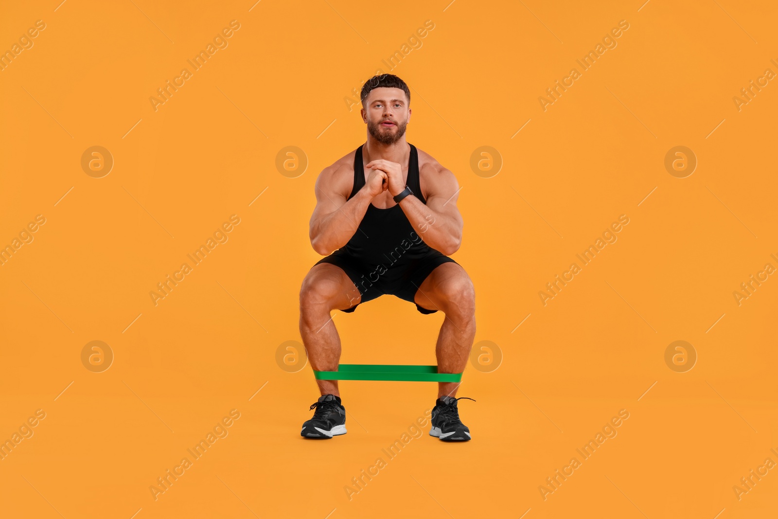 Photo of Young man exercising with elastic resistance band on orange background