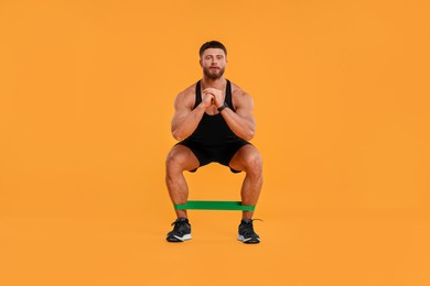 Photo of Young man exercising with elastic resistance band on orange background